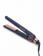 A navy blue flat iron hair straightener with rose gold accents, including the plates, trim button, and power cord base, shown on a clean white background.