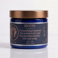 A blue jar of Biotin Hair Mask with a metallic bronze lid, set against a clean white background with a soft reflection.