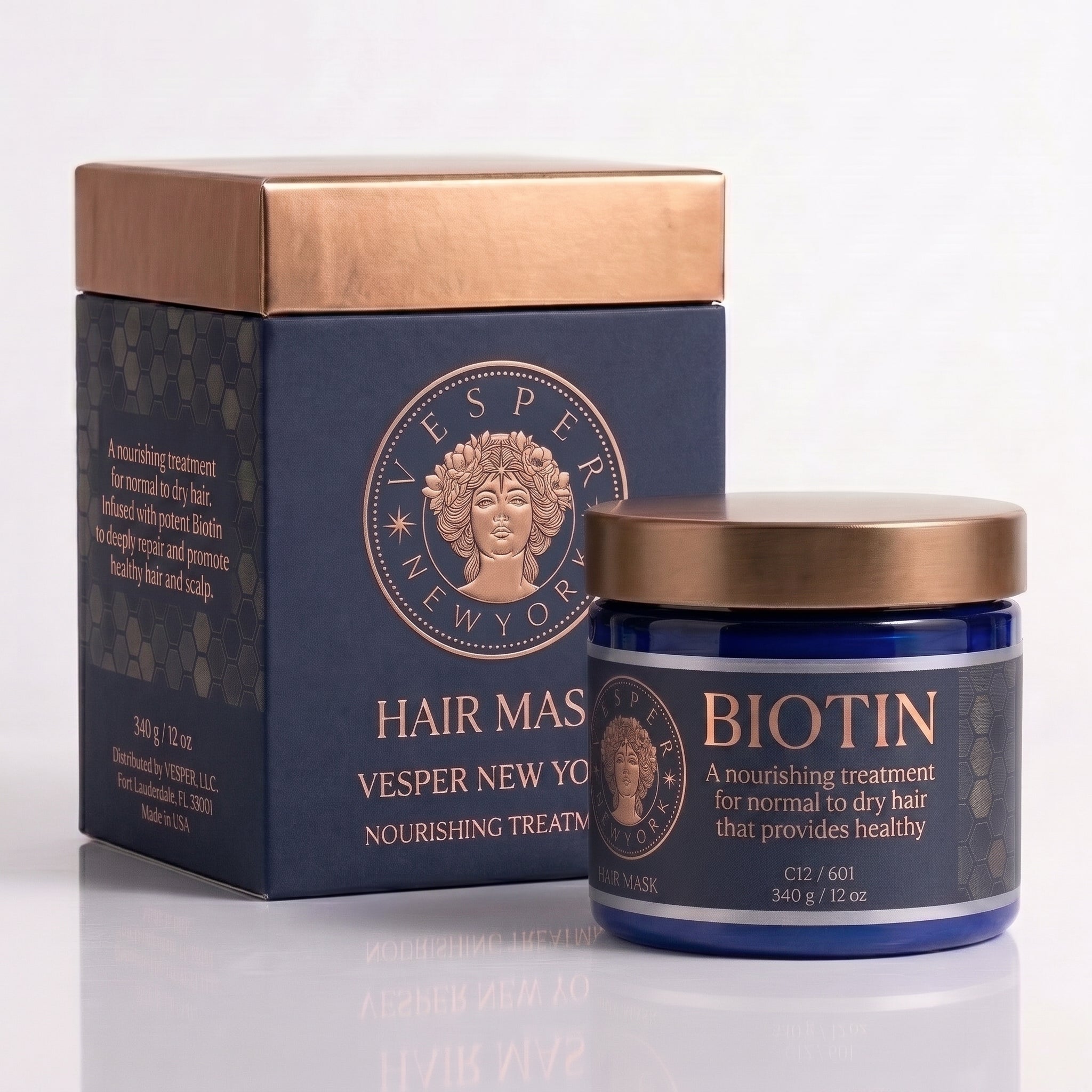 Vesper New York Biotin Hair Masque treatment shown with its navy blue box and matching jar featuring metallic rose gold accents and a gold lid, on a clean white background.